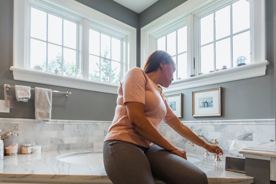 woman sitting on edge of tub with andersen awning windows in background